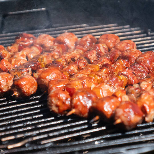 Spiedini misti di carne e verdure con salsa BBQ sfrigolano sulla griglia rovente per un catering a Trento.