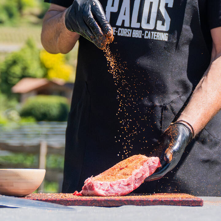 Un istruttore di corsi BBQ di Palos spezia un taglio di carne premium con un rub artigianale, preparandosi per una lezione a Trento.