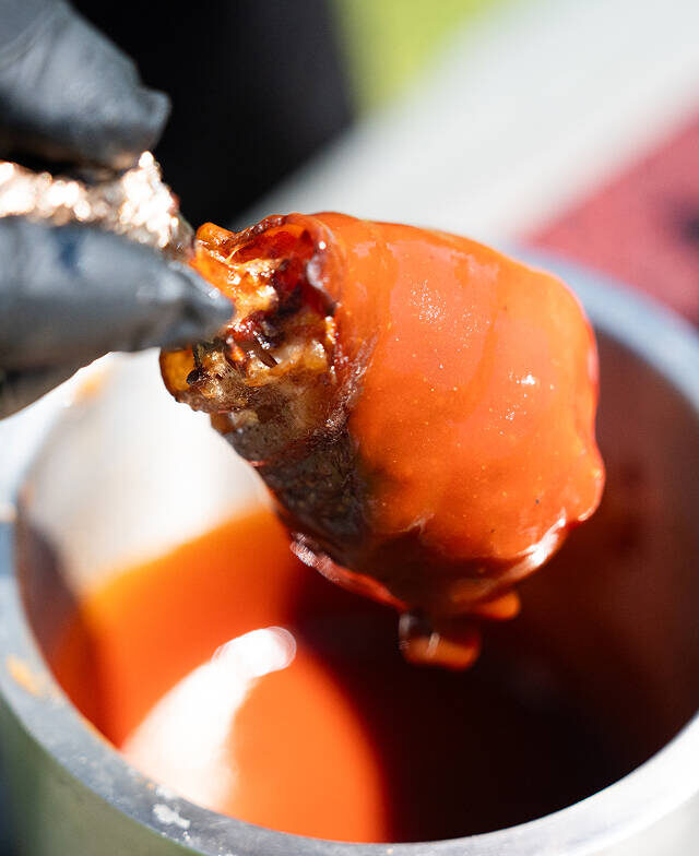Primo piano di un invitante bocconcino di carne appena intinto in una densa salsa per barbeque, preparato da un esperto durante un evento di catering a Trento.