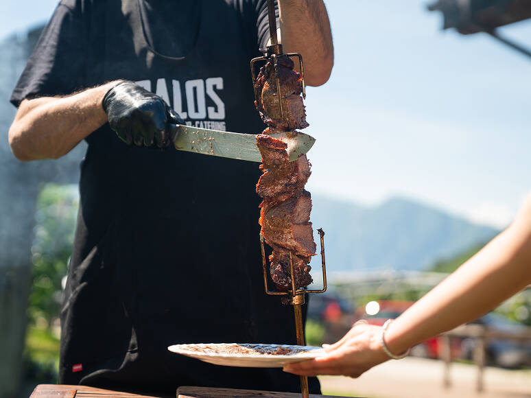 Uno chef di Palos affetta della carne arrosto da uno spiedo verticale direttamente nel piatto di un ospite durante un evento di catering BBQ all'aperto a Trento.