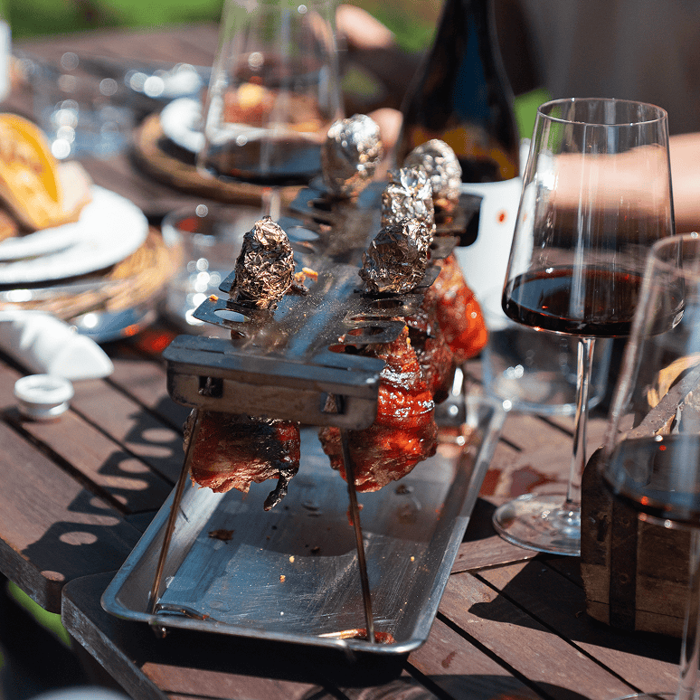 Dettaglio di un tavolo allestito per un catering BBQ a Trento, con spiedini di carne e calici di vino.