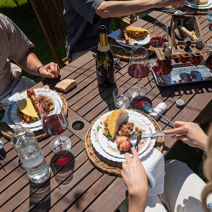 Tavola apparecchiata all'aperto per un catering BBQ a Trento, con piatti gourmet a base di carne e ospiti che pranzano.